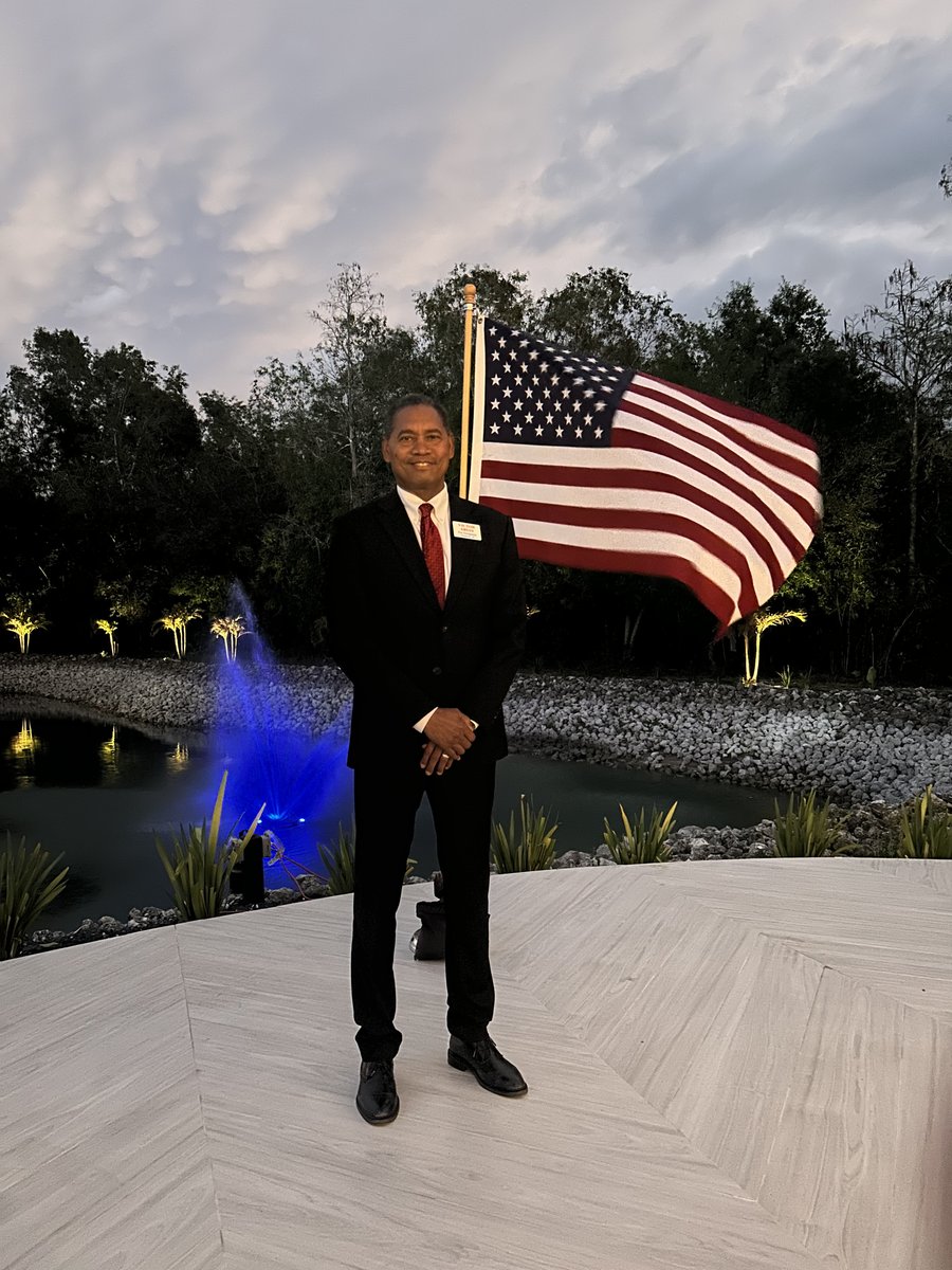 Victor Arias standing with the American flag at an evening community event in Southwest Florida