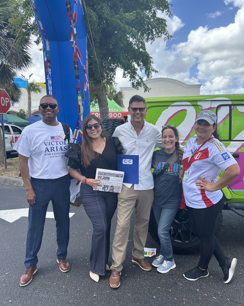 Victor Arias standing with four community members holding a local newspaper at the outdoor Feria Latina festival